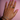 A hand with pink nail polish displays multiple rings and two bracelets against a pink background. The jewelry includes gold and diamond details, exuding elegance.