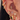 A close-up of a woman's ear adorned with a curated ear stack featuring multiple gold and crystal earrings. Highlights include a pink enamel bow charm hoop, a heart-shaped crystal drop hoop, star-shaped studs, and several pavé crystal hoops and cuffs in varying sizes and placements.