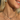 Close-up of a smiling woman wearing silver layered necklaces, including a paperclip chain with a pavé clasp, a star lariat chain, and a personalised necklace with the name "MEL" in sparkling letters. She also wears multiple silver earrings, including a floral dangle charm, in the warm glow of the sun.