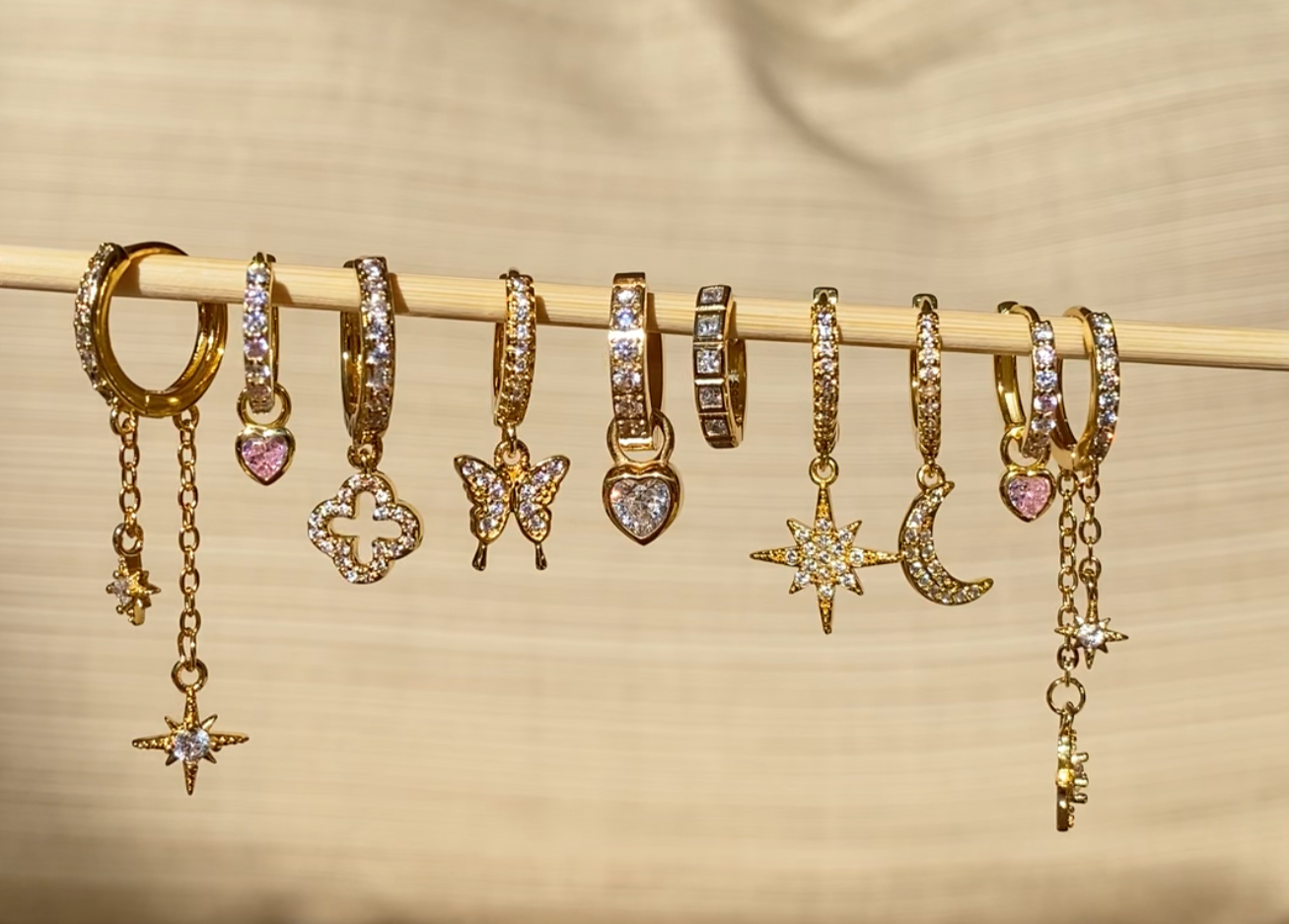Set of gold hoop earrings with various charms on a beige background