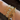 Gold bracelets with various charms on a wrist against a dark background