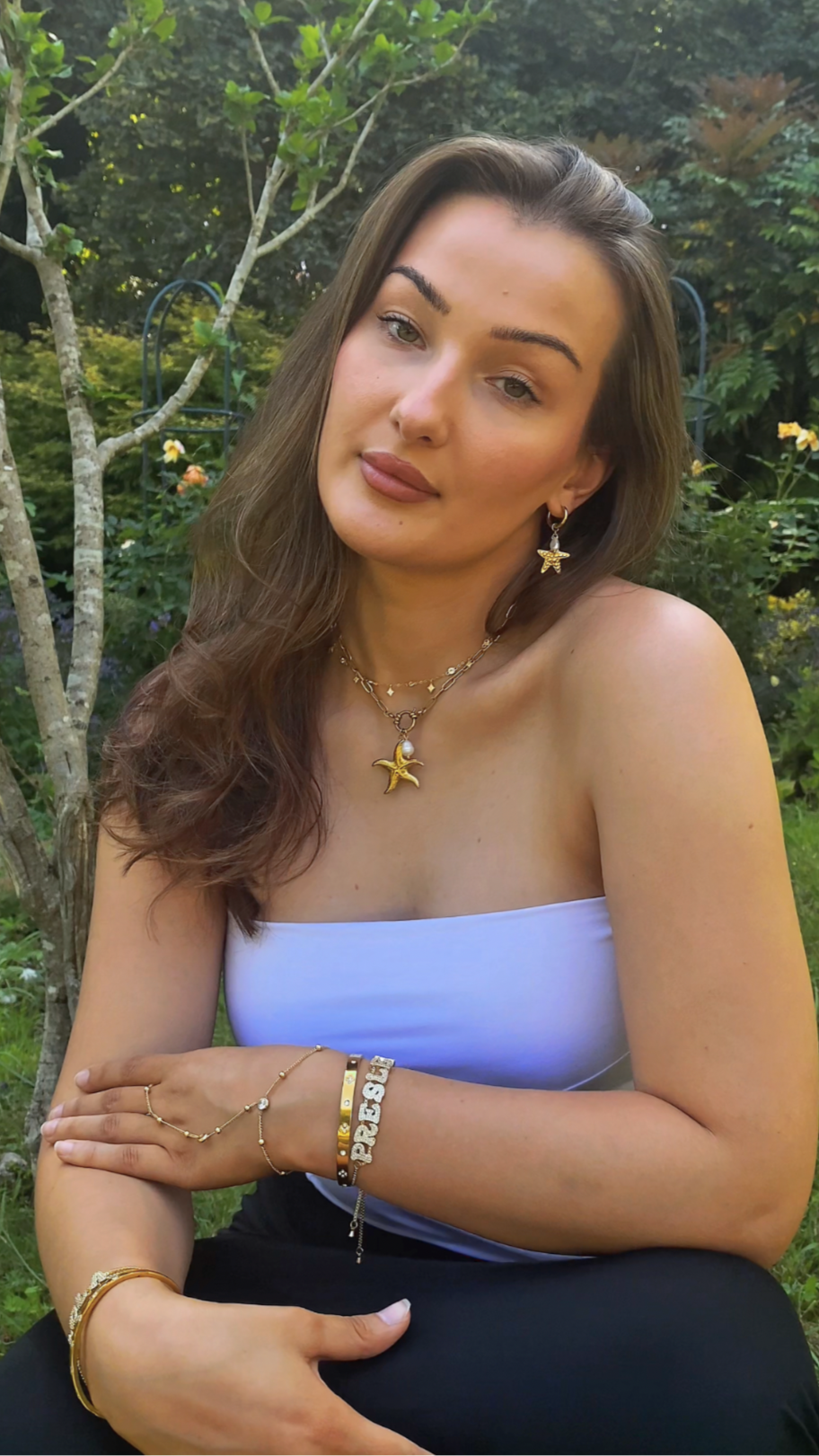 Woman sitting down, showing her necklace, bracelet, bangle, earrings and starfish themes. 