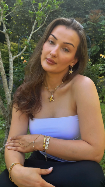 Woman sitting down, showing her necklace, bracelet, bangle, earrings and starfish themes. 